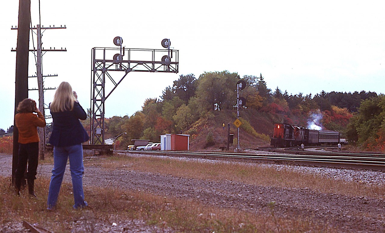 Well, Geez !!!!  About as rare as a Baldwin at Bayview..........I'm over on the south side at the Junction awaiting the passenger train and all of a sudden these two female railfans came running over.  Not to pass this up, I quickly switched from my 35MM lens to a 28 for a sneak shot. After the train passed, off they went and I never heard of them again.
The eastbound? Oh I did write 3121 on my slide, I guess that must be a GP9 trailing, but who cares? Had to keep my priorities in order.