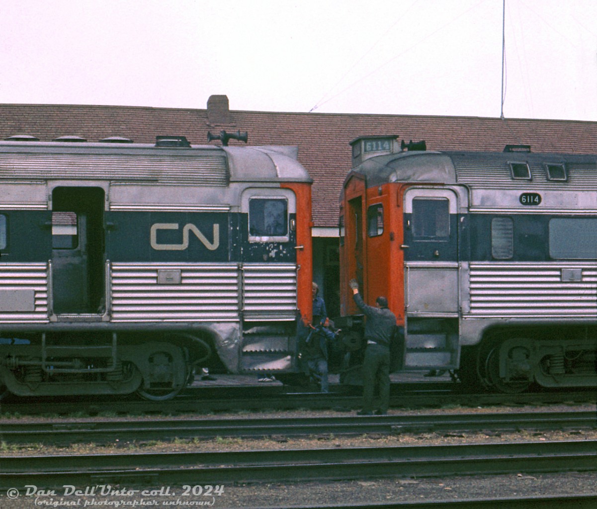 After pulling back out of the siding south of Camrose station, CN RDC-3 6356 (left) on the Calgary-Edmonton Railiner train inches up to the back of CN RDC-1 6114 (right), on the Drumheller-Edmonton Railiner. Crews work to connect both units together, and both trains will depart Camrose station together as a combined run to Edmonton. CN 6356 had previously arrived first at Camrose, but headed into the siding nearby to clear the station track for 6114 to arrive.There's a lesson in CN RDC spotting here: note 6356 on the left has the later "Phase 2" Budd RDC ends (headlight in housing built into the roof, numberboards at front face only) while 6114 has "Phase 1" ends that CN modified (original headlight position was above the doorway, moved to a new headlight housing on the roof with added numberboards in order to clear the diaphragm and diaphragm housings CN installed). CN also plated over the larger Phase 1 window openings and cut smaller Phase 2 windows into them. The original numberboards remained on the body sides. The fluting on the vestibule doors was unique to 6356, originally delivered to the MKT with end and vestibule door fluting (a styling feature CN didn't opt for). 6356 has a later Nathan K3L air horn, while 6114 has the earlier M3H model that CN (and CP) ordered standard on most of their early diesels.Original photographer unknown (possibly E.W.Johnson), Dan Dell'Unto collection slide.