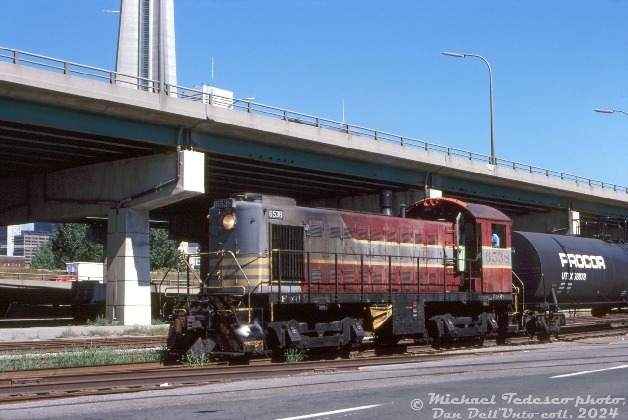 Canadian Pacific S3 switcher 6538, still painted in faded maroon & grey block paint, works the Toronto Harbour Commission trackage at Rees St. Yard, located along Queen's Quay at Rees St. Timetables indicate this is the "Central Harbour Terminals" area. By that time, GP7u, GP9u and SW1200RSu units were being rebuilt by CP to replace the old Alco/MLW switcher fleet.

CP S3 6538, built by MLW in 1955, was retired in 1985 and sold to Sidbec-Feruni in Quebec, becoming their 0409. It appears to have become Boston Railway Terminal 0409 (and eventually scrapped).

Rees Street yard was a small stub-ended yard along the THC trackage to serve the various industries along the Toronto harbourfront. East of the yard, the line had streetrunning and street-side running portions all the way to the lead coming from Don Yard. West of Rees Street, the line continued on a private right-of-way and curved north at Bathurst Street, past the old Loblaws warehouse to the main rail corridor (CN accessed the line there, and CP had their "Wharf Lead" from Parkdale Yard that connected to it). As time when on and waterfront industry declined, traffic dwindled, and in the mid-1980's the THC Queen's Quay trackage from Bathurst Street to near Yonge was removed, leaving the eastern trackage to serve Redpath and some other remaining industry.

Michael Tedesco photo, Dan Dell'Unto collection slide.