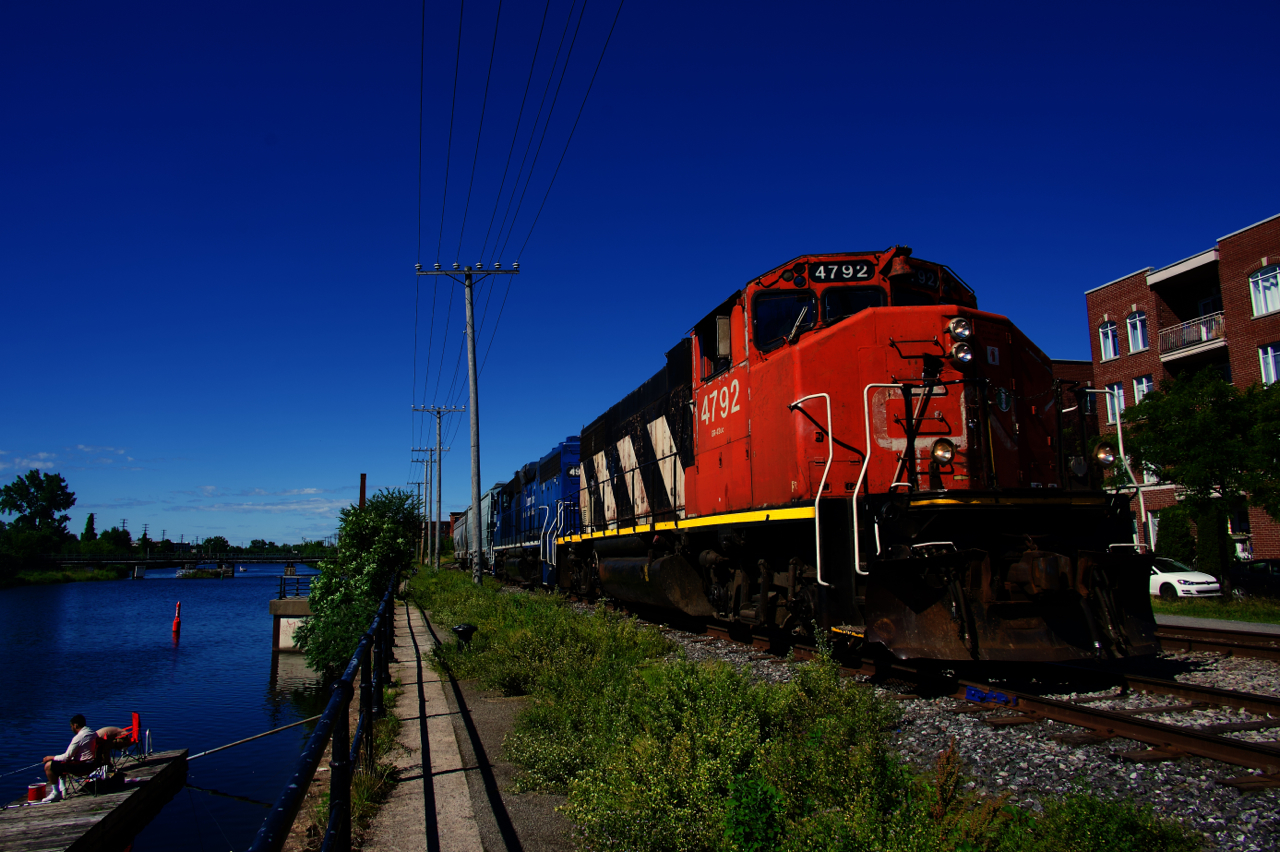 A couple of fishermen try their luck on the Lachine Canal as CN 500 shoves towards the main line with two grain empties from Ardent Mills. The CN Montreal sub crosses the canal using the bridge at far left.