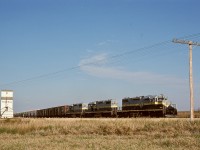 Northern Alberta Railways typically utilized three of their four SD38-2 units to handle the Great Slave Lake traffic down to and then up from a bridge across the Peace River at the town of the same name.  Here, on Friday 1976-09-24, that day’s GSL Turn is just starting to roll homeward again behind 402 + 404 + 401 after pausing for a mandatory standing train inspection after a hard grind upgrade from Peace River to level land at Judah, and now about to cross Township Road 825, with forty-one miles to Winagami Junction then one more to home terminal McLennan.  From there, two more subdivisions spread over 262 miles for the cars to reach Edmonton.