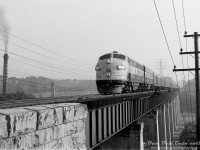 Another take on the famed Don River "Half-Mile Bridge": one year-old Canadian Pacific FP7 1401 (built as 4100 in 1953 but later renumbered/regeared for 89mph passenger service) leads a brand new 1900-series F9B southbound on the Don Branch on train #33, the overnight Pool train from Ottawa, sometime in the Spring-Summer of 1954. The time would be just before 7am, and Pool train <a href=http://www.railpictures.ca/?attachment_id=46919><b>#21 from Montreal with CP 1415 leading</b></a> wouldn't be too far behind. Nearby, smoke pours out from two of the four smokestacks for the brick kilns at the nearby Don Valley Brickworks. 
<br><br>
According to a September 1954 passenger timetable, Ottawa-Toronto Pool train #33 departed Ottawa Union Station at 11:00pm, made its way to Bedell, turned west to Smiths Falls, and continued west on the Belleville Sub until Glen Tay where it diverted via the Havelock & Peterborough Subs to Agincourt (#21 kept on the Belleville-Oshawa Subs), then back on the Oshawa Sub at Agincourt, and down the Don Valley branch portion from Leaside to Union Station. If today's train was running on time, it would be due at Don Station at 6:58am and Toronto Union at 7:10am (15 minutes ahead of the following #21 from Montreal).
<br><br>
Going off aerial photos, the intrepid unknown photographer would have had to plan this early morning shot and walk in from nearby Chester Hill Road, as there was <a href=https://www.toronto.ca/ext/archives/s0012/fl1953/s0012_fl1953_it0154.jpg><b>no Don Valley Parkway or Bayview Avenue</b></a> at this time - only the CN Bala Sub and a service road to the brickworks passed through the valley here (and, both on the other side of the Don River).
<br><br>
The 1400-number series was reserved for CP's special pool of 89mph-geared passenger GM cab units used on The Canadian, The Dominion and other passenger trains on the system. Icicle breakers would be added later in 1954. CP 1401 was part of the 1400-1404 group, which were late-production FP7's renumbered from 4099-4103. They were followed by brand a new order of FP9's numbered 1405-1415, and FP7's 1416-1434 renumbered from earlier 4000-series units. The passenger B-unit pool was similar: brand new F9B's 1900-1907, and renumbered F7B's 1908-1919. The higher-speed gearing reduced their tonnage rating in freight service, and many were later regeared back to 65mph and renumbered to their old 4000 & 4400-series numbers in the 1960's for better power utilization as CP was discontinuing many of its passenger train services (reportedly, the 89mph gearing wasn't needed as much on CP's lines out east as it was out west).
<br><br>
The original 1401 pictured here met its end when it hit a washout at Terrace Bay while leading The Canadian in 1965, and was traded to GMD on a new GP35. Decades later, CP would christen a <a href=http://www.railpictures.ca/?attachment_id=49941><b>second 1401</b></a> (former CN FP9 6541) when it purchased an ABA set of F-units to power its Royal Canadian Pacific train in 1998.
<br><br>
<i>Original photographer unknown, Dan Dell'Unto collection negative (large-format scanned with a DSLR).</i>