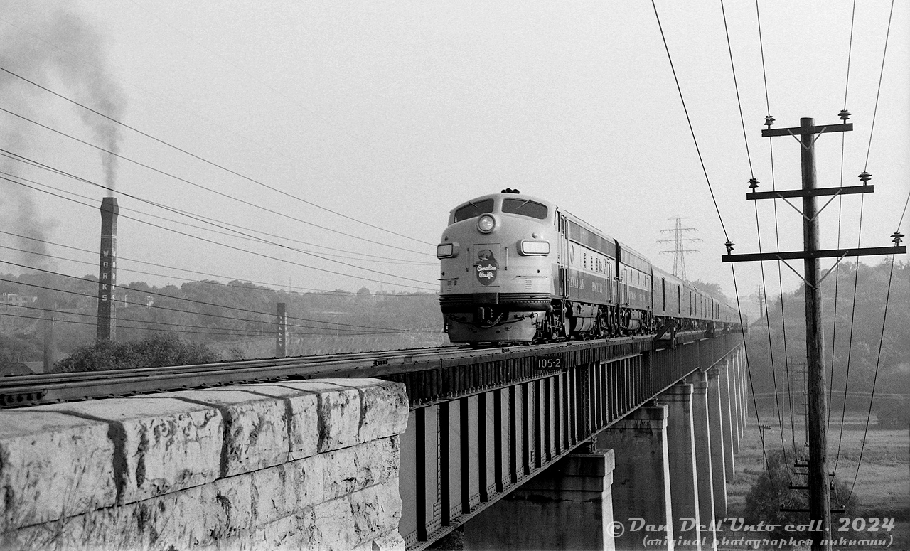 Another take on the famed Don River "Half-Mile Bridge": one year-old Canadian Pacific FP7 1401 (built as 4100 in 1953 but later renumbered/regeared for 89mph passenger service) leads a brand new 1900-series F9B southbound on the Don Branch on train #33, the overnight Pool train from Ottawa, sometime in the Spring-Summer of 1954. The time would be just before 7am, and Pool train #21 from Montreal with CP 1415 leading wouldn't be too far behind. Nearby, smoke pours out from two of the four smokestacks for the brick kilns at the nearby Don Valley Brickworks. 

According to a September 1954 passenger timetable, Ottawa-Toronto Pool train #33 departed Ottawa Union Station at 11:00pm, made its way to Bedell, turned west to Smiths Falls, and continued west on the Belleville Sub until Glen Tay where it diverted via the Havelock & Peterborough Subs to Agincourt (#21 kept on the Belleville-Oshawa Subs), then back on the Oshawa Sub at Agincourt, and down the Don Valley branch portion from Leaside to Union Station. If today's train was running on time, it would be due at Don Station at 6:58am and Toronto Union at 7:10am (15 minutes ahead of the following #21 from Montreal).

Going off aerial photos, the intrepid unknown photographer would have had to plan this early morning shot and walk in from nearby Chester Hill Road, as there was no Don Valley Parkway or Bayview Avenue at this time - only the CN Bala Sub and a service road to the brickworks passed through the valley here (and, both on the other side of the Don River).

The 1400-number series was reserved for CP's special pool of 89mph-geared passenger GM cab units used on The Canadian, The Dominion and other passenger trains on the system. Icicle breakers would be added later in 1954. CP 1401 was part of the 1400-1404 group, which were late-production FP7's renumbered from 4099-4103. They were followed by brand a new order of FP9's numbered 1405-1415, and FP7's 1416-1434 renumbered from earlier 4000-series units. The passenger B-unit pool was similar: brand new F9B's 1900-1907, and renumbered F7B's 1908-1919. The higher-speed gearing reduced their tonnage rating in freight service, and many were later regeared back to 65mph and renumbered to their old 4000 & 4400-series numbers in the 1960's for better power utilization as CP was discontinuing many of its passenger train services (reportedly, the 89mph gearing wasn't needed as much on CP's lines out east as it was out west).

The original 1401 pictured here met its end when it hit a washout at Terrace Bay while leading The Canadian in 1965, and was traded to GMD on a new GP35. Decades later, CP would christen a second 1401 (former CN FP9 6541) when it purchased an ABA set of F-units to power its Royal Canadian Pacific train in 1998.

Original photographer unknown, Dan Dell'Unto collection negative (large-format scanned with a DSLR).