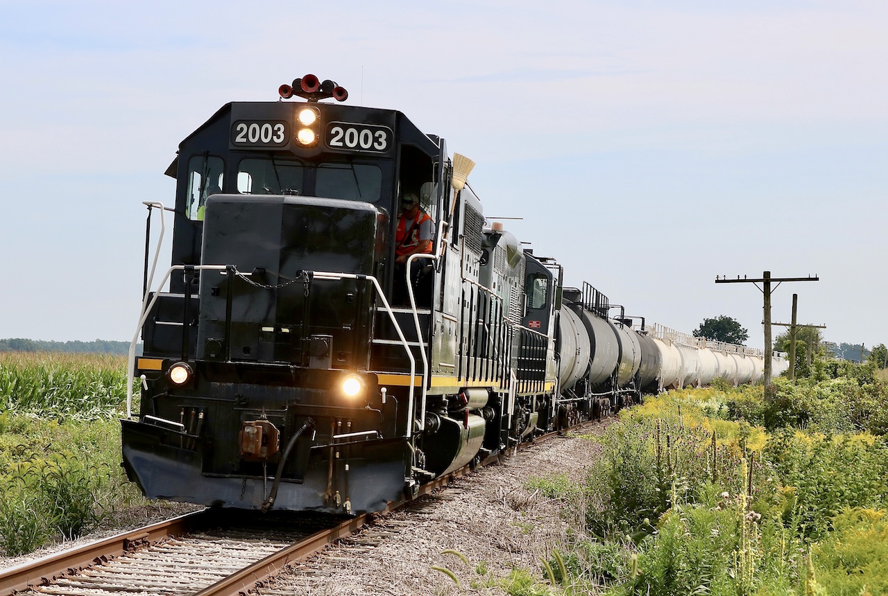 Deep in Amish country basic black paint just seems to set the tone as borrowed LDS GP38 2003 and GP9U 1597 haul a decent size cut of tank cars  westward near Orwell. The old telephone pole date back to when this line was a mainline connecting St. Thomas to the Niagara region, hosting not just CN train but those of NS and its predecessors. Sadly today most of the line is gone, and what remains is in need of serious upgrades that may never come. Much of GIO Rails trip requires constantly watching for defective or non operating crossings. But it appears business is gradually picking up. It’s unfortunate the traffic and elevators in Courtland are gone today leaving what remains of the line east of Tilsonburg quiet and overgrown. While GP38 2003 looks like a standard GP38 it is a little unique as it was one of a small group of GP38’s built for Penn Central with dual control stands. This upgrade includes an extended front window arrangement.