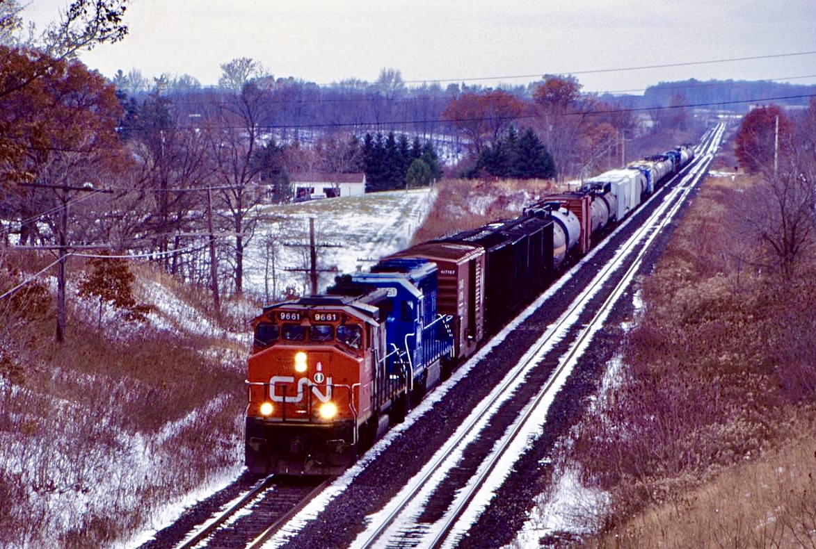 Back when it seemed GP40’s ruled the rails. Back in the mid CN and CP we’re both dealing with motive power shortages. Often leading and borrowing foreign units. Along with a group of NS C30-7’s, CN also borrowed a group of Conrail SD45-2. There was no mistaking the units considering they all had oversized fuel tanks. I believe some are still roaming NS rails today. Here a short eastbound with CN GP40-2W 9661 and borrowed Conrail SD45-2 6661 are heading towards Paris West after crossing the Nith River well in the distance. There is a bit of a clash of the seasons going on with snow and left over fall colours.