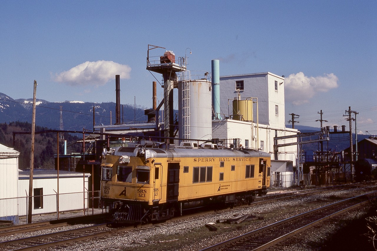 The bright yellow Sperry Rail Service rail inspection cars were always a camera treat, and on Tuesday 1982-03-16, SRS 123 was no exception as it slowly and steadily tested westward on the North track of CP’s Cascade sub. at mileage 119.2, past the Allied Chemicals (now Chemtrade Solutions) plant on the south shore of Burrard Inlet between Port Moody and Vancouver.