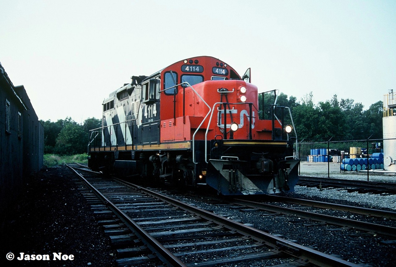 On a humid August evening, the CN 15:30 Kitchener Job has cut away from their cars they brought to Elmira, Ontario and are pictured running around them at the end of track of the Waterloo Spur. Shortly, GP9RM 4114 will begin switching the customers in Elmira, before heading back to Kitchener with darkness eventually overtaking the southbound train.