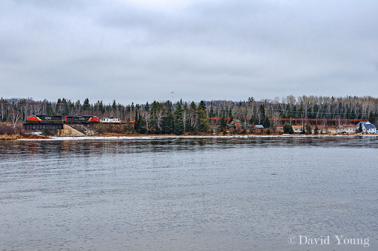 Seen looking across from the point on Mackenzie Bay along the shore of Lake Superior we see the second load of rail from the Kinghorn crossing over the mouth of the Mackenzie River. The white Operation Lifesaver caboose following CN 5713 and CN 2522 stands out against the stark and dull trees of a late northern Ontario, while the loaded train of rail just seems to blend in. Not the same effect as a mixed freight loaded with paper, lumber and the like but it will have to do. Rail removals crews would reach this location by July 2009 and have since made things much safer for area fisherman who like to fish beneath the bridge. They may not have the worry of trains to contend with anymore however when those that like to load 5 gallon buckets of smelt up in the springtime, its a long walk out without the support of the smooth rail to drag the heavy pails back to their vehicles.