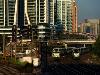 A pair of inbound GO Transit trains are heading towards nearby Union Station at about the same speed.