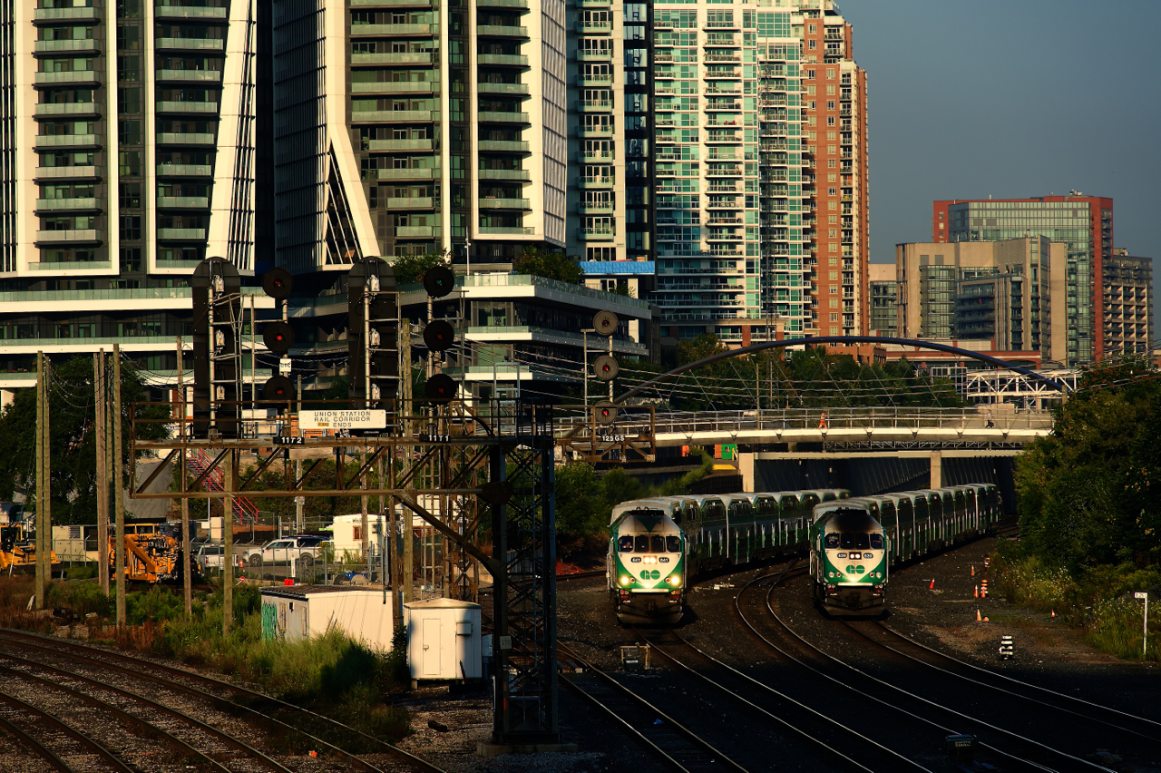 A pair of inbound GO Transit trains are heading towards nearby Union Station at about the same speed.