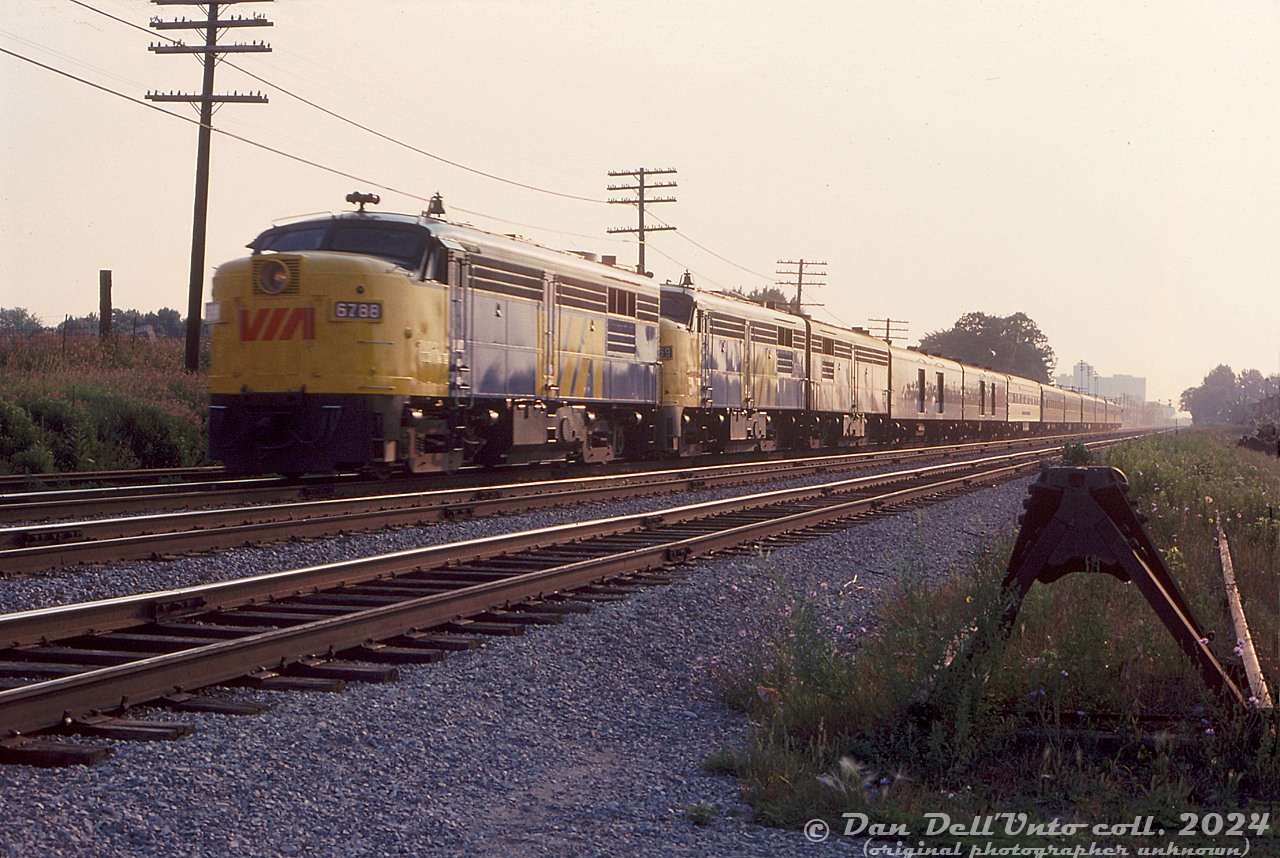 A morning westbound VIA passenger train speeds through Scarborough with three MLW's on the head-end: FPA4 6788 and 6769, sporting VIA paint and logos, and an unknown 6800-series FPB4 still in CN zebra stripe paint. Nine passenger cars trail, including two baggage cars (most appear to still be in CN paint, as the new "VIA" branding was barely two years old at this point).

The location is just before Greenwood Avenue on CN's Kingston Sub. As per track diagrams, the train is heading westbound on the "west mainline", with the next track over the "east mainline", then the Y-200 service track, and the track bumper at the end of the old Greenwood Avenue team track (Y-012, appears to be out of use at this point). North of the mainline track was another service track, Y-230, that lead into TTC's Greenwood Yard nearby.

Original photographer unknown, Dan Dell'Unto collection slide.