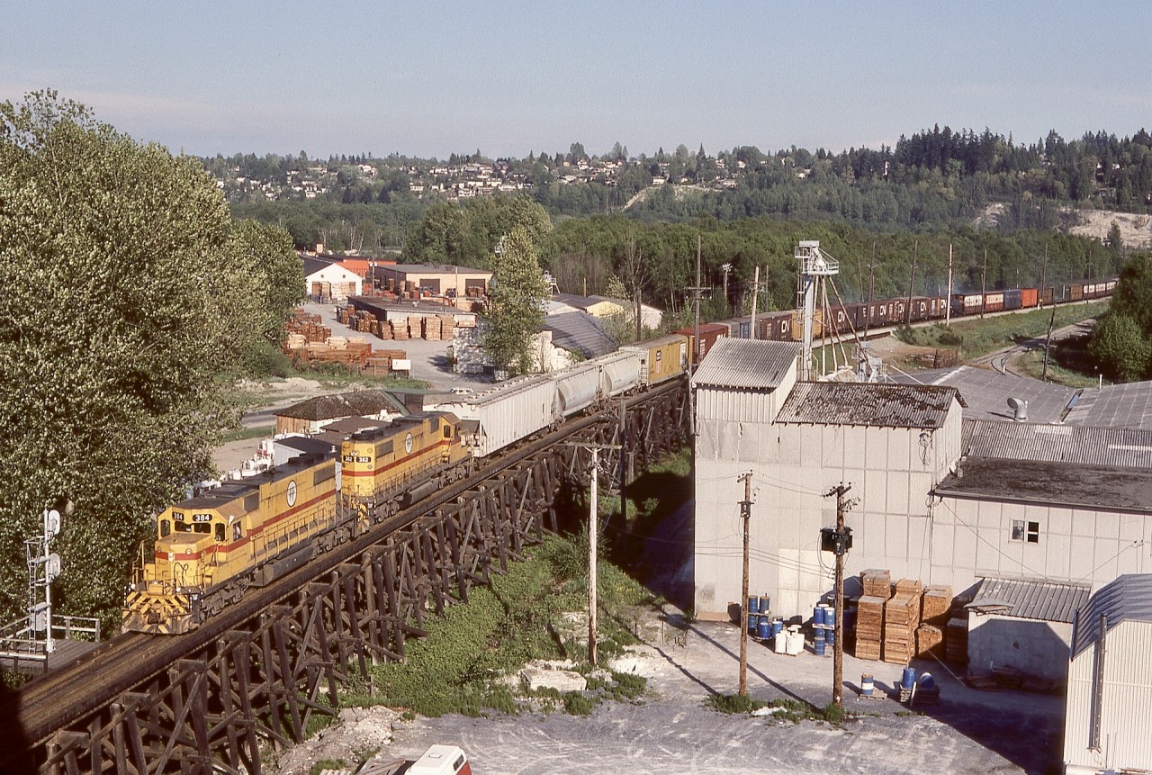 A pair of EMD SD38-2s, BC Hydro 384 and 382, brought a regular westward Valley Freight down Scott Hill and paused at the interlocking signal for the Fraser River Bridge to cross into New Westminster on Sunday 1982-05-09 at 1802 PDT, as seen here from the Patullo highway bridge sidewalk (ear plugs very handy for reducing road traffic noise).

This view was lucky timing for me, as twenty days later on 1982-05-26, a major fire involving the swing span of that Fraser River railway bridge completely disrupted local railway operations on BCH, CN, CP, VIA, and Amtrak, providing many photo opportunities when all rail traffic was detoured via a bridge from Mission City to Matsqui.