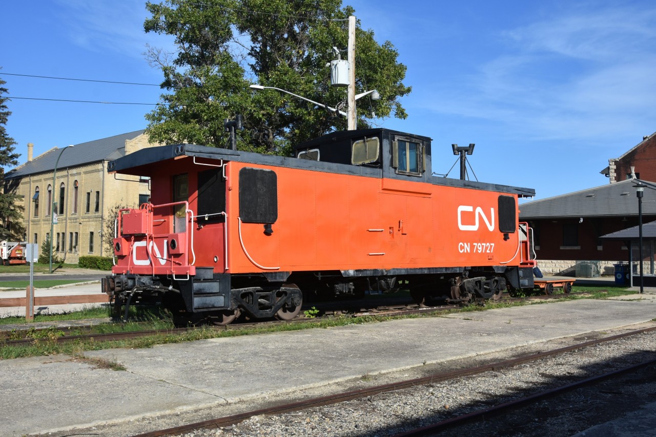 Two-tone paint 
CN 79727 is a CN PSC built (9/1974) mainline caboose that is now on static display at the VIA Rail station/Dauphin Railway Museum in Dauphin, MB, Mile 121.7 CN Gladstone Sub., Mile 0.0 CN Togo Sub. 
The van has been vandalized over the years requiring the wire mesh window protectors. Track inspection lights, step lights, and other appliances have been destroyed and still require repair/replacement. 
Hopefully a fresh paint job is in the works in the not-too-distant future.