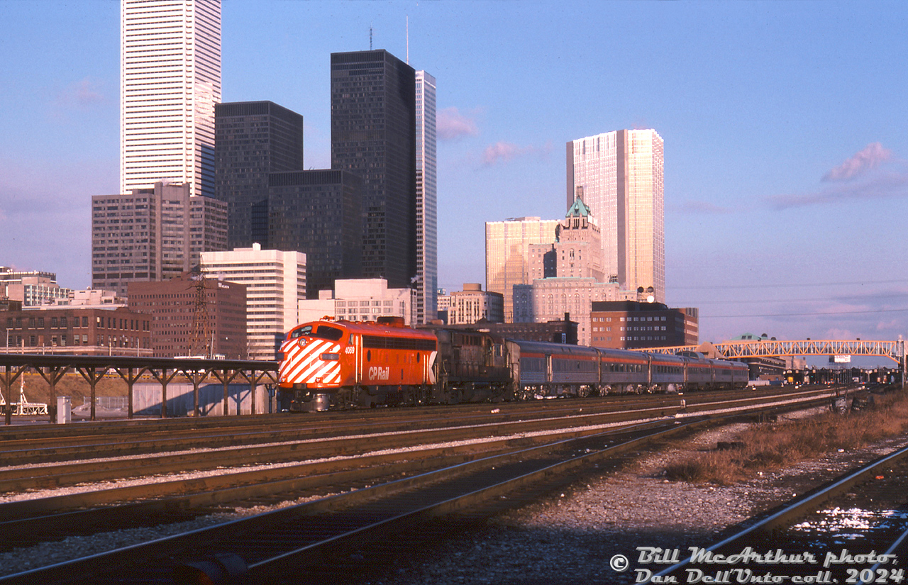 Departing downtown Toronto in the low December late afternoon/early evening light, CP Rail train #11 "The Canadian" (Toronto-Sudbury leg) passes by John Street interlocking tower (visible behind the Skyline dome) and the old CN freight loading platforms as it makes its way through the downtown Toronto Terminals Railway trackage to CP's Galt Sub at Bathurst Street. Lead unit is CP FP7 4069, sporting bright "Action Red" paint with later 8" striping. Trailing is steam generator-equipped RS10 8478 in very ratty maroon & grey "Script" paint. A short consist of six stainless steel Budd cars follow (no Park car this late in the game for #11/12).

All the usual suspects are in attendance in this pre-condo boom photo of Toronto's downtown skyline: the TD, BMO and RBC towers, CP's Royal York Hotel, the brown CNCP Telecommunications building at 151 Front Street, and Union Station off in the background beyond the new yellow CN Tower pedestrian bridge.

Bill McArthur photo, Dan Dell'Unto collection slide.