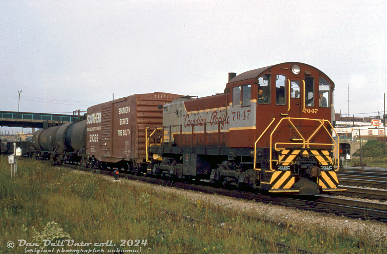 Canadian Pacific 7047, a little 1000hp Alco S2 switcher built in 1946 and assigned to John Street Roundhouse nearby, rumbles through the Toronto Terminals Railway corridor at Spadina Avenue with a short local freight or transfer move, heading eastbound towards Union Station. Its duties today could be numerous depending on assignment, as CP worked industries downtown along Queen's Quay, the Portlands, and also interchanged traffic with CN at Don Yard and Cherry Street.

Original photographer unknown, Dan Dell'Unto collection slide.