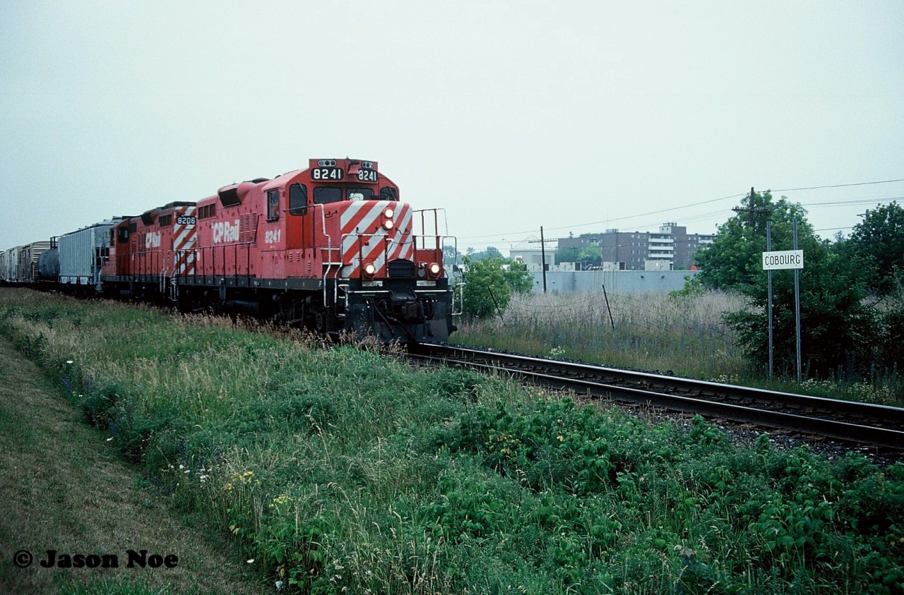 During a hazy and humid summer afternoon, the CP Cobourg Turn is viewed heading back westbound to Toronto, Ontario after completing it’s work at Cobourg. The turn is seen passing the Cobourg station name sign with GP9u’s 8241 and 8206.