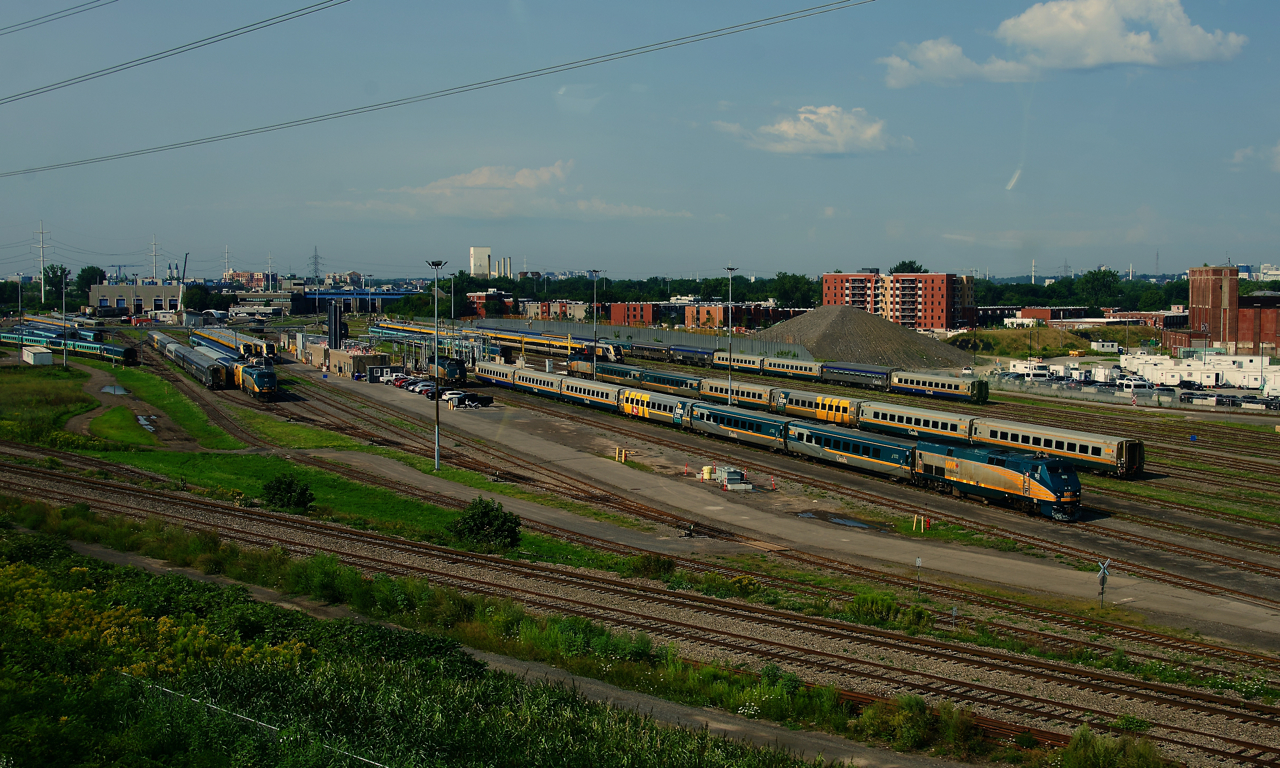 A variety of VIA Rail equipment is seen at the Montreal Maintenance Centre from a passing REM train.