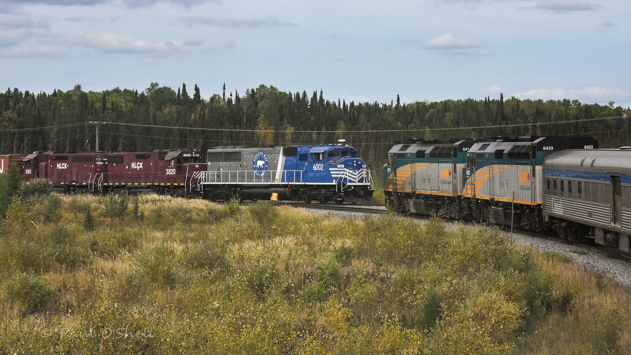 Meeting at the wye  
The Hudson Bay Railway way freight has just entered the north leg of the wye at Thompson Jct. with VIA 693 The Hudson Bay holding the south leg, waiting it's turn to take the 30 mile trip up HBR's Thompson Sub. to the VIA station at Thompson, MB. 
A headend crew member from the passenger train does a roll-by inspection of the lengthy freight train, and will then walk several hundred feet to line the switch, allowing VIA 693 to proceed. 
The way freight consist this day was a very interesting mix of fuel tank cars, general freight boxcars and gons, trucks and construction equipment on flats, and a string of HBRY ballast cars. It was nice to see one of HBRY's newer locomotives on the point. 
The only thing absent from this photo is a ray of sunshine. :-( 
A big thank you to my friend Benny for editing this photo.