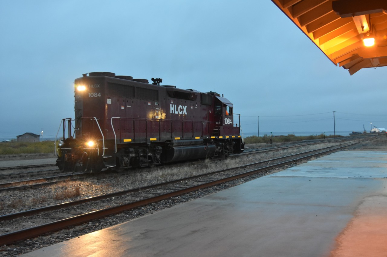 Service appointment required  
HLCX 1084 is in front of the station in the yard at Churchill, MB in a steady, light rain switching cars from the inbound way freight, and marshalling others from the ramp tracks that will be departing on tomorrows southbound run. 
A ditch light bulb needs to be replaced on the rear of the locomotive at the next service opportunity.