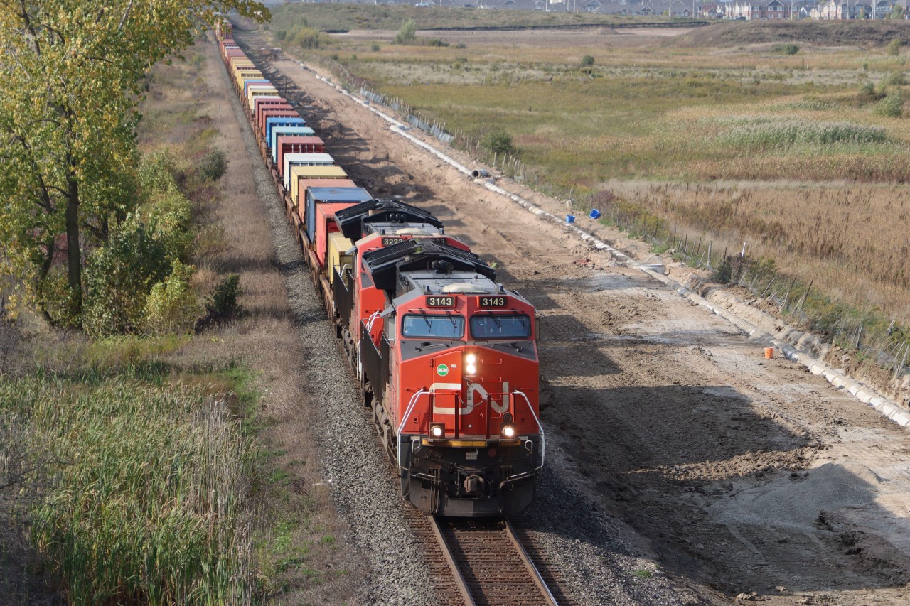 Westbound Intermodal train is about to pass under Britannia Road and knock down the signal at Ash. Preparatory works continue for the second main track between Ash and Derry part of the construction works for the future CN Milton Logistic Hub.