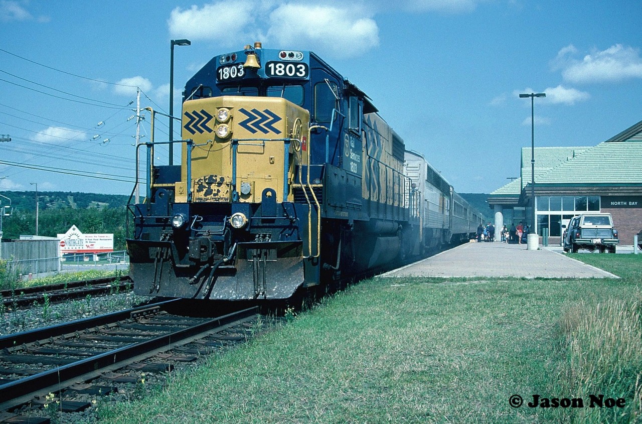 During an August afternoon, the station platform is bustling with passengers as Ontario Northland Railway train 698 prepares to depart North Bay, Ontario with GP38-2 1803 leading to Toronto.