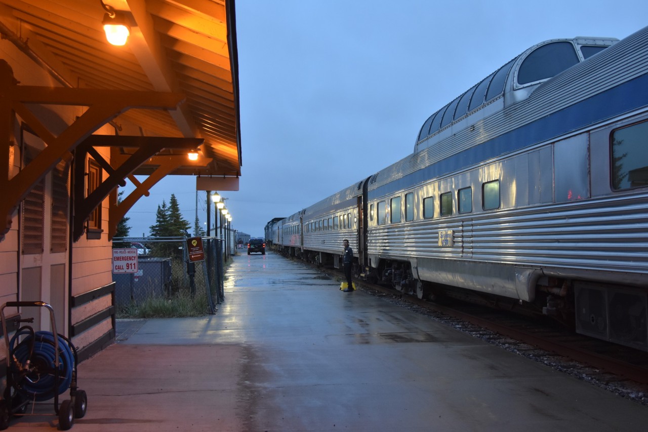 ALL ABOARD  
Skyline car attendant Sean stands by the step box at the vestibule door of economy coach VIA 8130 at the Churchill station waiting for the last of the economy class passengers to board VIA 692 The Hudson Bay. 
The baggage truck can be seen driving down the platform after loading all the luggage and supplies for the southbound journey. 
I enjoyed a full day in the town of Churchill, and the rain was kind enough to hold off until a half hour before boarding.
The consist for this evenings train is: 
VIA 6419 locomotive 
VIA 6433 locomotive 
VIA 8602 baggage car 
VIA 8118 economy coach 
VIA 8130 economy coach 
VIA 8511 Skyline dome 
VIA 8224 Chateau Roberval sleeping car