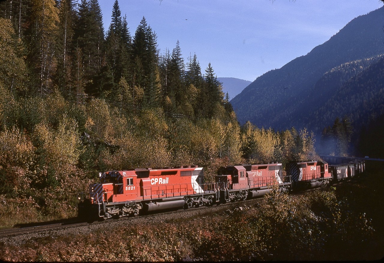 West of Revelstoke by 21.6 miles and a bit over a mile east of the east switch of Taft, CP and the Eagle River and the TransCanada Highway were squeezed through a small gap, and by climbing a gravel bank, a view excluding the highway was possible.  On Sunday 1974-10-13 at 1211 PDT, that worked well for a westward loaded Coleman coal train (note cross-hoppers with bottom-dump doors rather than bathtub rotary-dump gondolas) with all-SD40-2 power CP 5821 + 5660 + 5618.