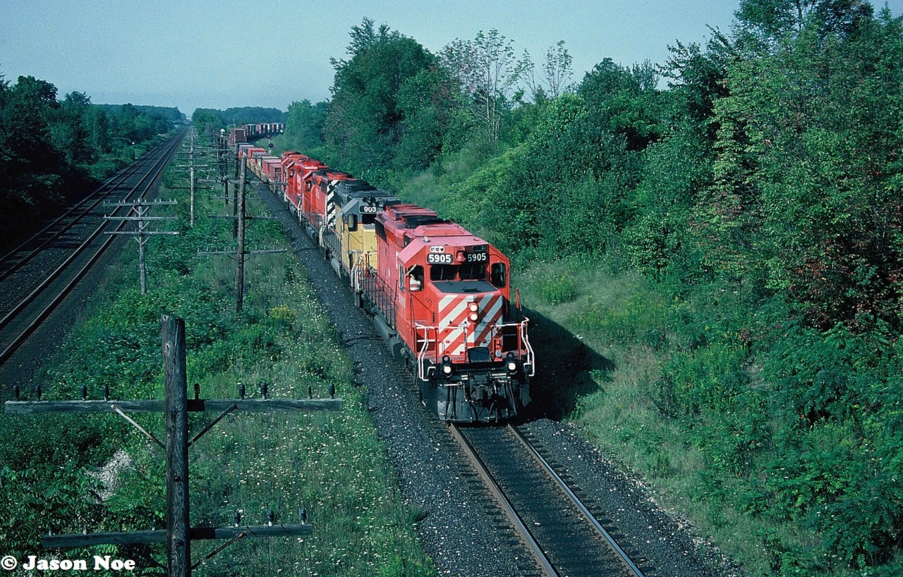 An eastbound CP intermodal train is seen passing through Lobo, Ontario as it approaches the Denfield Road overpass, west of London on the Windsor Subdivision. The consist has a variety of SD40-2’s in various CP paint schemes, including leased GATX SD40-2 903.