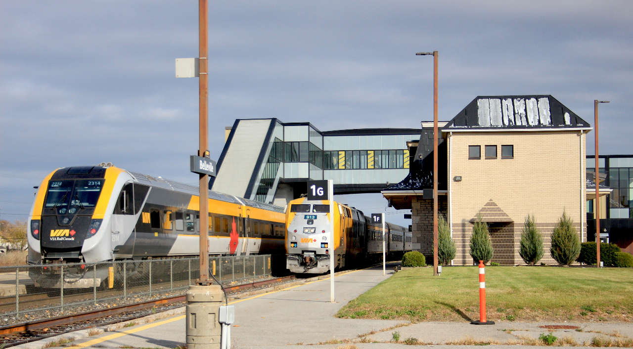 VIA Rail is going West with the old and East with the new. A Halloween afternoon at Belleville Station has VIA Rail Corridor Service train #42 with new Venture Trainset 2213/14 to Ottawa waiting on Track 2. VIA Rail Corridor Service train #53 led by 913, rolls in on track 1 on time. #42 was late by 15 minutes allowing for the meet. The old stone Belleville station in the foreground is overshadowed by the new glass and steel structure in the background.