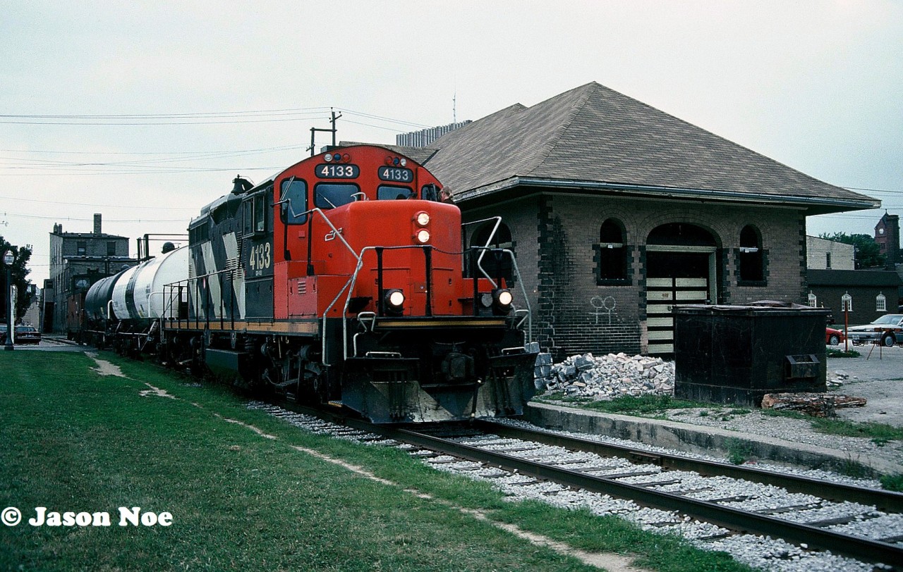 CN GP9RM 4133 leads the 15:30 Kitchener Job through downtown Waterloo, Ontario on the Waterloo Spur as they return from Elmira with two tanks and a caboose. At the time, the Waterloo Grand Trunk station to the right of the train was undergoing an extensive cosmetic restoration. A year later the station received it’s historic building status.