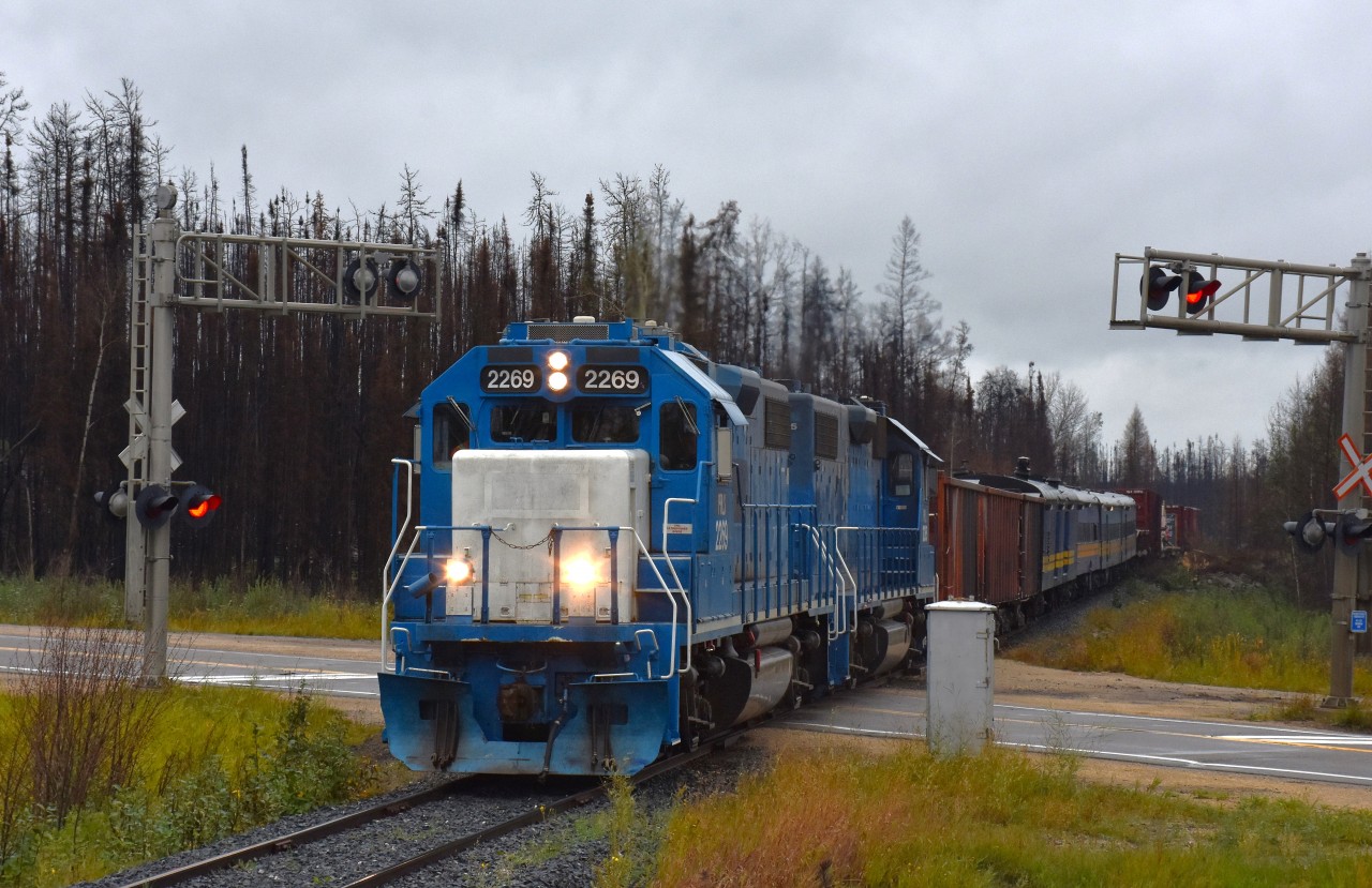 Unfortunately, I suppose, it was a bit of a downer to be up in these northern parts of Manitoba on a day that was drizzly and dull.  But on the "bright" side, this shot otherwise would have been almost directly into the sun.
Twice weekly Keewatin Railway's mixed train runs from The Pas to Pukatawagan, an isolated town that relies on the railroad for its very existence. The Mixed brings supplies, building materials, vehicles as well as an opportunity for some of the town folk to ride it back south to The Pas for shopping trips.
 In this view, PRLX 2269 and 2265 power the Mixed across Manitoba highway #10 (route to Flin Flon) as it heads northward after a stop at Cranberry Portage to pick up three gons and a few passengers.