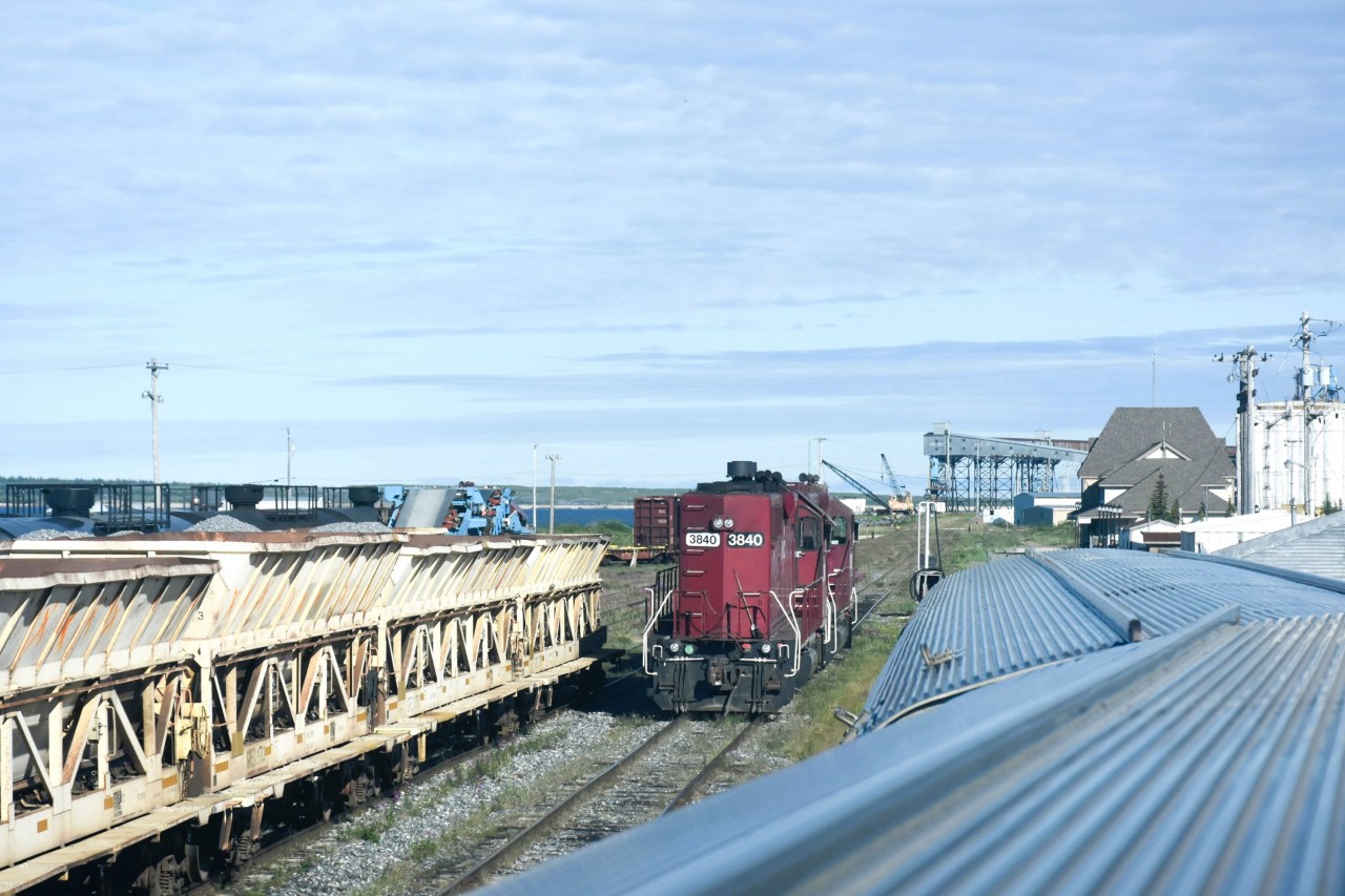 Heterochromia  
Bi-eyed number boards on HLCX 3840 stand out quite nicely on this beautiful sunlit August morning. 
As VIA 693 The Hudson Bay slowly reverses onto the station track at Churchill, MB I was able to catch quite a selection of revenue and OCS rolling stock in the HBRY yard. 
Nearby in the background, the Port of Churchill grain silos and elevators wait in silent anticipation for the opportunity to be reactivated at some date in the not-too-distant future.