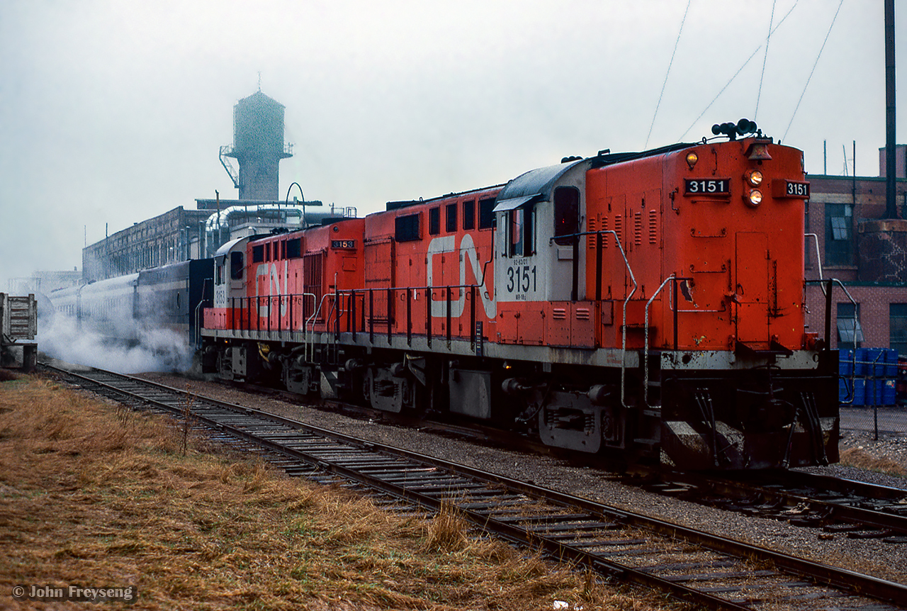 A pair of CN Tempo RS18ms idle away in the rain at Elmira while passengers of the seven car train have alighted to sample the sweet tastes of the Elmira Maple Syrup Festival.

Scan and editing by Jacob Patterson.