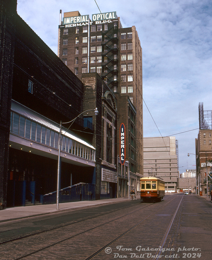 TTC Peter Witt streetcar 2766, operating on a fantrip during its early "Tour Tram" career, heads southbound on Victoria Street between Dundas and Shuter, passing the back of the old Imperial Six theatre (built as the Pantages Theatre in 1920, currently named the CAA Ed Mirvish Theatre) and the Imperial Optical building. In the background, Ryerson Polytechnical Institute's tan-coloured Podium (POD)/Library building is visible beyond Dundas at Gould.

Tom Gascoigne photo, Dan Dell'Unto collection slide.

On the same day at Parliament & Dundas: http://www.railpictures.ca/?attachment_id=53755