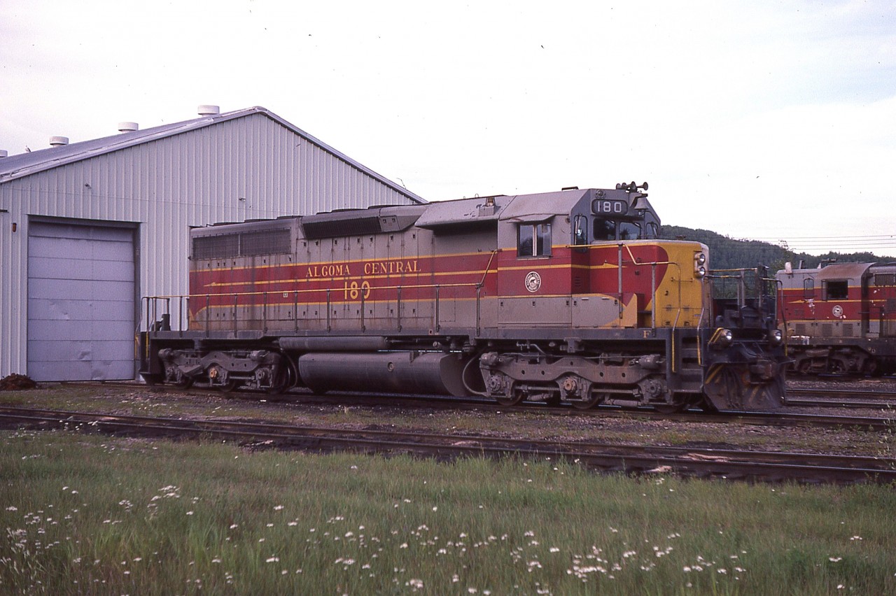 Algoma Central #180 sits outside the relatively new shop building in Hawk Junction. This unit would be around another 5 years or so before scrapping after being involved in a wreck.
I do miss the days of the AC. The area, now under CN is more like a desolate wasteland compared to back in the times I visited in the 70s & 80s.
An article I found on-line states that this unit was lost due to a derailment in 1980 caused a rail at mile 4  being removed by section men who had been fired by the company. This was how they showed their 'appreciation'.  Since I shot this image in 1985, I am thinking the date in the report was erroneous, instead of 1980 the incident probably occurred May 14, 1990.