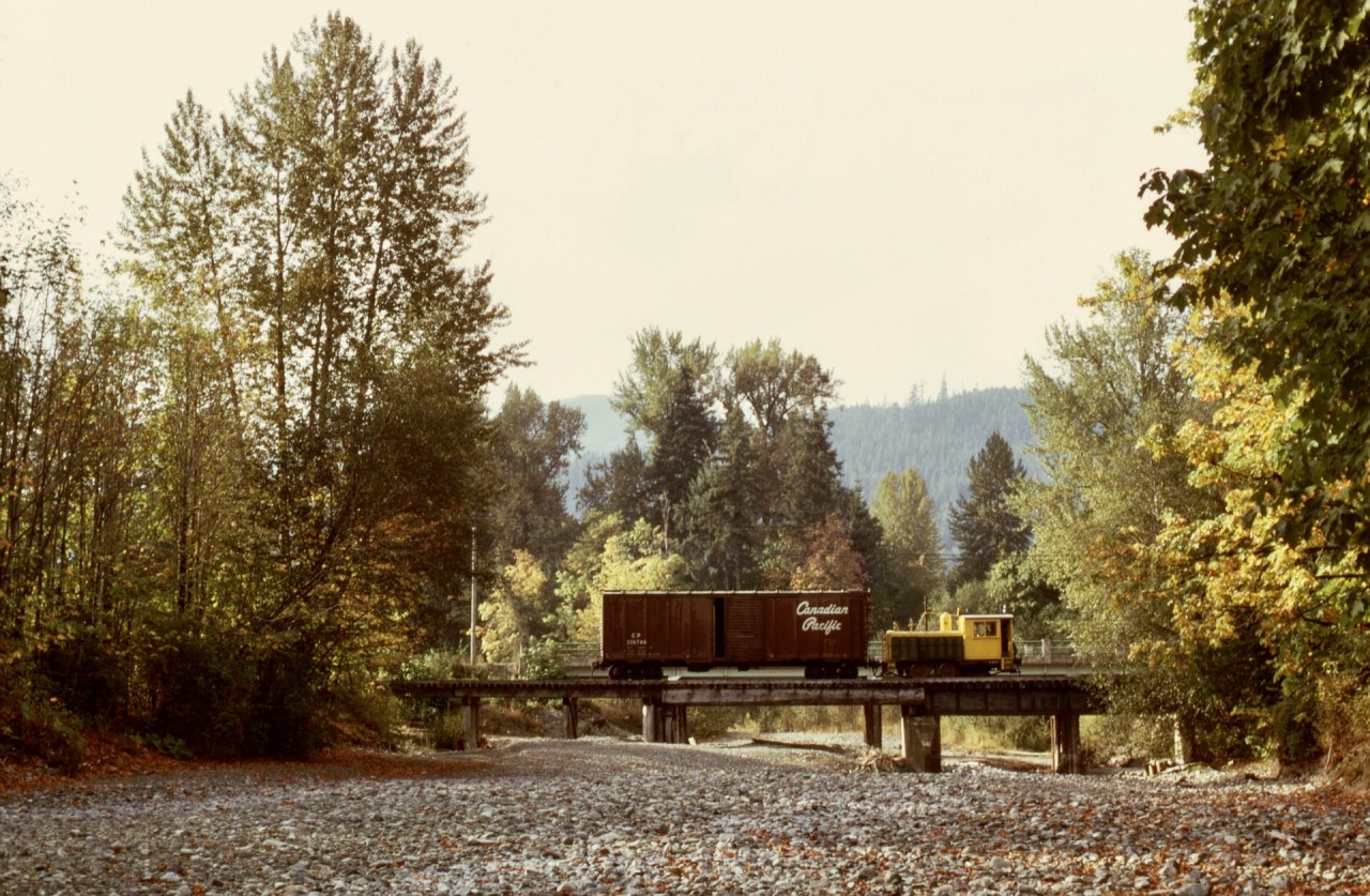 On Vancouver Island between a CP interchange at Lake Cowichan and a sawmill at Honeymoon Bay, Western Forest Industries operated a six-wheel Plymouth WLG3 (serial 3365 built 1929-11) numbered 40 (previously 7), and on Tuesday 1973-10-02, it picked up one empty boxcar from the interchange, seen here westward crossing over the Robertson River with three miles to go to reach home base.

Remarkably, that locomotive survives today at ninety-five years old, after serving for Westcan Terminals at Ogden Point in Victoria, now on display at the Kaatza Museum in Lake Cowichan, only three and one-half miles east of this photo location.