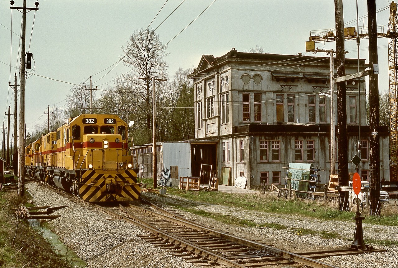 From New Westminster, BC Hydro ran a daily Valley Freight to the U. S. A. border interchanges at Huntingdon, regularly using three (and occasionally four) of their SD38s for power.  On Monday 1977-04-18, SD38-2 units 382 + 383 + 384 were in command, shown here passing the former BC Electric Railway substation at Coghlan just before crossing 256th Street.