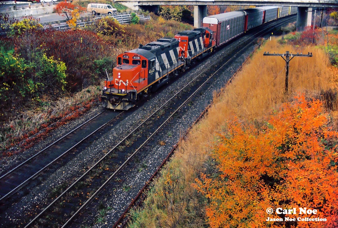 Carl Noe’s trusty plumbing van looks on as CN GP9RM’s 4128 and 4143 power a westbound local approaching Bayview Jct. in Burlington, Ontario on the Oakville Subdivision.