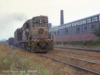 Canadian Pacific RSD17 8921, the "Empress of Agincourt", works her usual assignment hauling a large transfer freight, stretching down to Bathurst Street bridge, through the Parkdale area at Strachan Avenue grade crossing. The train has just come down <a href=http://www.railpictures.ca/?attachment_id=33301><b>CP's Don Branch</a></b> from Leaside, passed through the Toronto Terminals Railway corridor and <a href=http://www.railpictures.ca/?attachment_id=16615><b>Union Station downtown</b></a>, and is approaching <a href=http://www.railpictures.ca/?attachment_id=35550><b>CP's Parkdale Yard</b></a>. After its Parkdale visit, it will proceed to West Toronto/Lambton yards and then back to Agincourt Yard.<br><br>CP 8921 was originally built by Montreal Locomotive Works in 1957 as their only RSD17 model (essentially a Canadian version of Alco's RSD15). After demonstrating on CP, CN, and PGE, CP purchased demonstrator unit and numbered it after its series of FM/CLC Train Masters (<a href=http://www.railpictures.ca/?attachment_id=40661><b>8900-8920</b></a>). An oddball on the roster, it found a home in the Toronto area handling <a href=http://www.railpictures.ca/?attachment_id=6317><b>transfer duties</b></a> between CP's freight yards around the city, a task well-suited to the 2400 horsepower 6-axle unit. At the time of this photo, 8921's dirty and faded maroon and grey block lettering paint wasn't long for this world, and she would soon head to Montreal and emerge from Angus Shops in December 1973 sporting fresh action red and multimark paint (and return back to Toronto in time for the new year). Chop-nosed in 1988, 8921 lasted into the mid-90's but was retired due to cracks in her truck frames, and was donated to the <a href=http://www.railpictures.ca/?attachment_id=13444><b>Elgin County Railway Museum</b></a> in 1997.<br><br>The old Canadian Patent Scaffolding Company building, off Ordnance Street in the industrial Liberty Village/Parkdale area of Toronto, would survive until 2014/15-ish when gentrification saw it torn down for condos. Strachan Avenue itself would be <a href=http://www.railpictures.ca/?attachment_id=45668><b>grade-separated</b></a> by Metrolinx/GO Transit in the early 2010's.<br><br><i>Original photographer unknown, Dan Dell'Unto collection slide.</i>