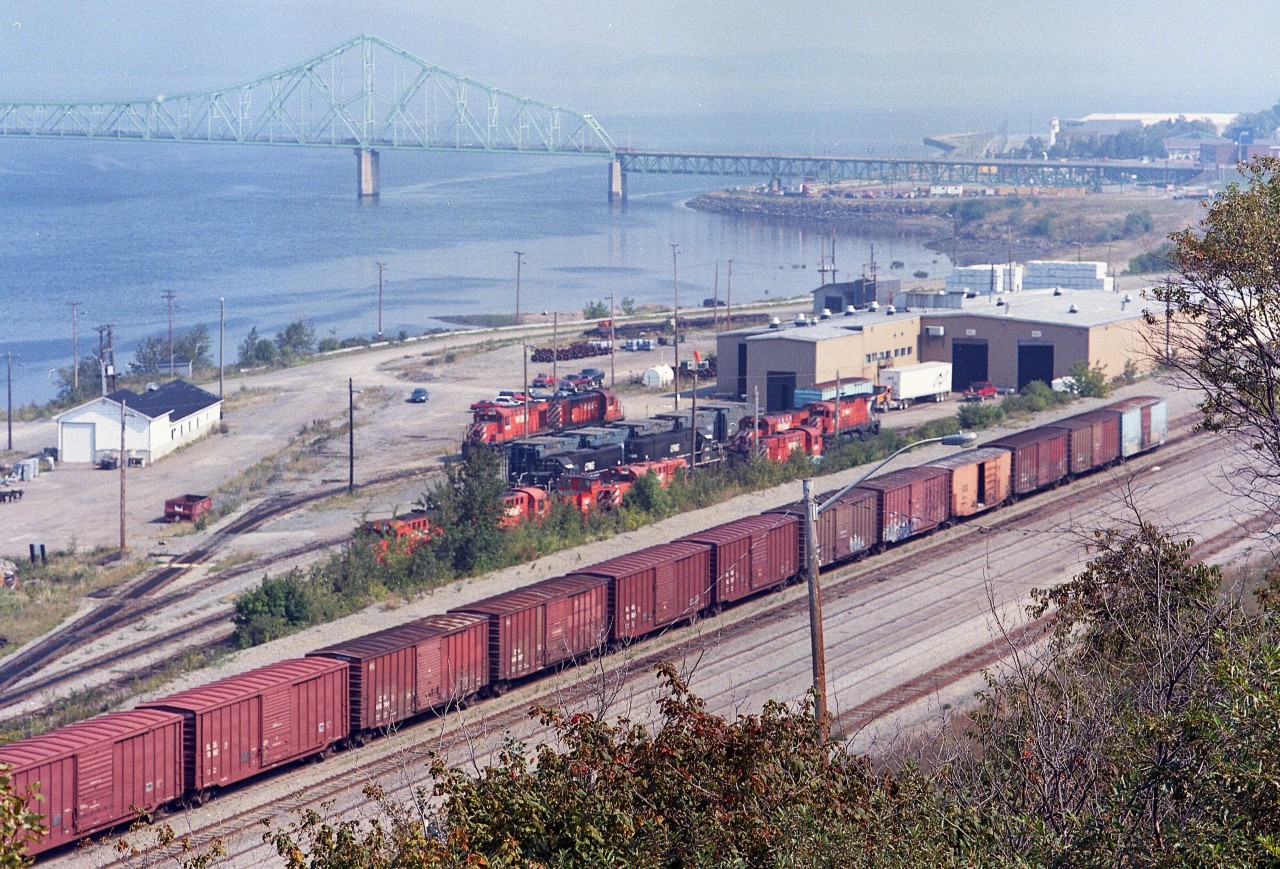 An overview of the New Brunswick East Coast Railway engine facilities and shop. The NBEC came about in early 1998 as CN gave up their ownership to Quebec Railway Corp, which operated the NBEC until 2008 when CN made a deal with Quebec Railway Corp and took back several railroads as well as this one.
The NBEC operated with a slew of x-CP RS-18u locomotives and later took on a half dozen x-CP C-424s as well as the same number of former CN SD40s.  The shop must have been kept busy keeping those old CP relics alive.
In the background is the J.V. Van Horne bridge, which spans the Chaleur Bay to Pointe-a-la-Croix, Quebec on the far shore.