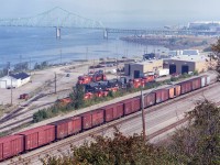 An overview of the New Brunswick East Coast Railway engine facilities and shop. The NBEC came about in early 1998 as CN gave up their ownership to Quebec Railway Corp, which operated the NBEC until 2008 when CN made a deal with Quebec Railway Corp and took back several railroads as well as this one.
The NBEC operated with a slew of x-CP RS-18u locomotives and later took on a half dozen x-CP C-424s as well as the same number of former CN SD40s.  The shop must have been kept busy keeping those old CP relics alive.
In the background is the J.V. Van Horne bridge, which spans the Chaleur Bay to Pointe-a-la-Croix, Quebec on the far shore.