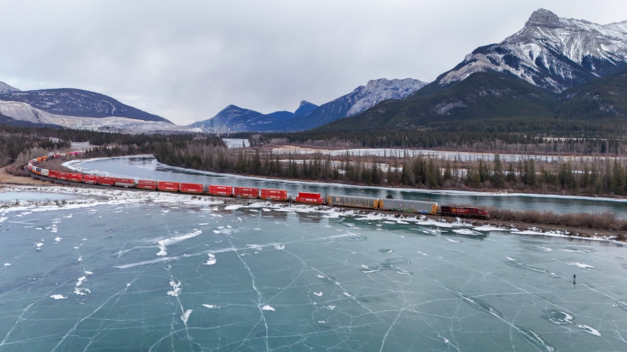 Winter in the Rockies.  CPKC 105 highballs towards Gap, as someone skates on Gap Lake, just west of Exshaw.