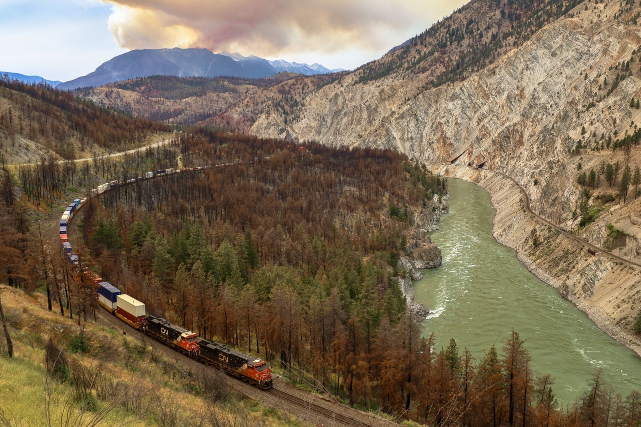 The Lytton area was devastated by a wildfire in the summer of 2020, and the canyon still wears the scars of the fire, with scorched trees and brush along the right of way.  Two years after this fire we catch CN Q 10451 02 rolling down the CP Thompson Sub, as another fire rages in the mountains above Lytton, creating overcast conditions on an otherwise sunny day in the canyon.