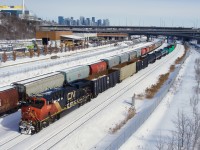 The conductor waves as CN 305 passes parked grain cars.