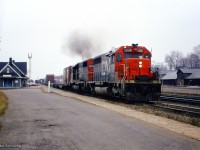 After setting off a cut of hoppers (seen just above the red car's hood,) CN Extra 5028 east thunders past the station at Ingersoll for points east.  Though hard to see, an SW1200RS is in the yard beyond the train order signal.
<br><br><i>Scan and editing by Jacob Patterson.</i>