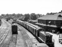 Hamilton - Owen Sound train 173 pulls into Palmerston behind brand new GMD SW1200RS 1317, built in August 1958.  People on the platform take in the sight of the new locomotive, diesels only appearing in Palmerston during the previous two years, and primarily MLW RSC13s.  Eight cold steam locomotives sit in the distance beyond the passenger equipment, while other RSC13s are seen around the yard.  

<br><br>Above the RPO car, CNR 1732 stands on the Newton Sub, possibly the power for mixed train M331 to Kincardine, whose coach is spotted out of frame on the stub track at right.  Sitting just slightly in the frame ahead of 1317 is the tail end of mixed train M329 for Southampton, behind CNR 1722.  After 173's 1120h departure, both M331 and M329 will depart at 1135h.  The mixed trains will arrive back at Palmerston at 1525h and 1530h respectively, giving passengers half an hour until the 1600h arrival of 174 for Hamilton.

<br><br><i>Original Photographer Unknown, Jacob Patterson Collection Negative.</i>