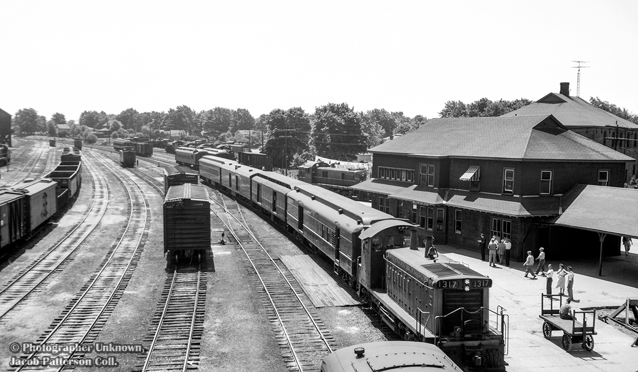 Hamilton - Owen Sound train 173 pulls into Palmerston behind brand new GMD SW1200RS 1317, built in August 1958.  People on the platform take in the sight of the new locomotive, diesels only appearing in Palmerston during the previous two years, and primarily MLW RSC13s.  Eight cold steam locomotives sit in the distance beyond the passenger equipment, while other RSC13s are seen around the yard.  

Above the RPO car, CNR 1732 stands on the Newton Sub, possibly the power for mixed train M331 to Kincardine, whose coach is spotted out of frame on the stub track at right.  Sitting just slightly in the frame ahead of 1317 is the tail end of mixed train M329 for Southampton, behind CNR 1722.  After 173's 1120h departure, both M331 and M329 will depart at 1135h.  The mixed trains will arrive back at Palmerston at 1525h and 1530h respectively, giving passengers half an hour until the 1600h arrival of 174 for Hamilton.

Original Photographer Unknown, Jacob Patterson Collection Negative.