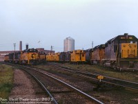 A gaggle of second-generation EMD road power congregates on the yard tracks at Chesapeake & Ohio's St. Thomas shops, including plenty of GP30's, GP35's, and GP40-2's in earlier C&O blue & yellow bookend paint and later Chessie System "circus" colours. Readable units are C&O 4168, 3539, 3560 and 4176, and cabooses 3663, 3664?, 3529, 3507 and 3528 are parked among them. The <a href=http://www.railpictures.ca/?attachment_id=22731><b>roundhouse and turntable</b></a> are out of view to the right. Scenes like this at St. Thomas would vanish in the next decade, as C&O's facilities here would be abandoned in the mid-80's and demolished (the roundhouse bays and turntable pit on the former property are still visible in aerial imagery today).
<br><br>
<i>Original photographer unknown, Dan Dell'Unto collection slide.</i>