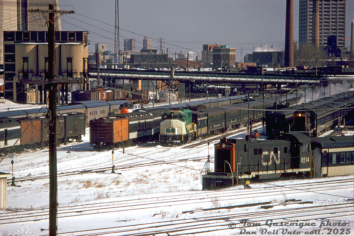 A mixed-bag of equipment sits at CN's Spadina Coachyard west of the roundhouse shop area in February 1974: in the center is a pair of GO Transit GP40-2W's (9809 on the closest end) bracketing a set of Ontario Northland Polar Bear Express passenger cars and a CN steam generator (possibly equipment leased by GO during the winter months?). Some of CN's MLW S13 units that switched the coachyards are in attendance shuffling black and white passenger equipment around, including CN 8514.

Railway Express Agency and Merchants Dispatch (MDT) yellow ice reefer cars are mixed in with CN passenger equipment. Tempo cars are visible on the left, and a Turbo Train set is also in attendance. Beyond the old steam-era coaling tower, the Spadina Avenue bridge can be seen, base of the CN Tower (then still under contruction), CN Spadina roundhouse, City of Toronto water filtration plant buildings, some harbourfront grain elevators, the Toronto Star office tower at 1 Yonge Street, and the TTR Central Heating Plant.

Walls of condos have since replaced much of the railway scene here.
Tom Gascoigne photo, Dan Dell'Unto collection slide.