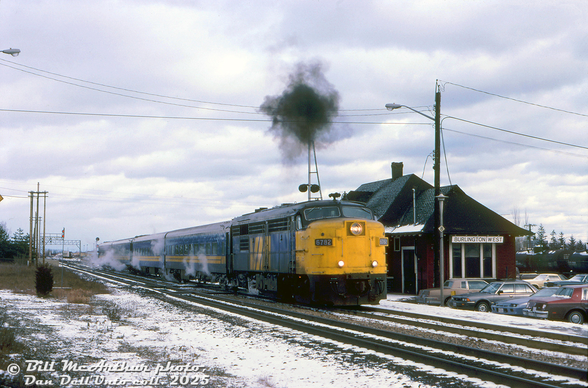 VIA FPA4 6782 coughs up a ball of black Alco smoke, presumably departing the VIA/CN Burlington West station after its stop on westbound train #73 from Toronto. Four blue and yellow coaches follow, steam heat escaping from their underframe components.

Bill McArthur photo, Dan Dell'Unto collection side.